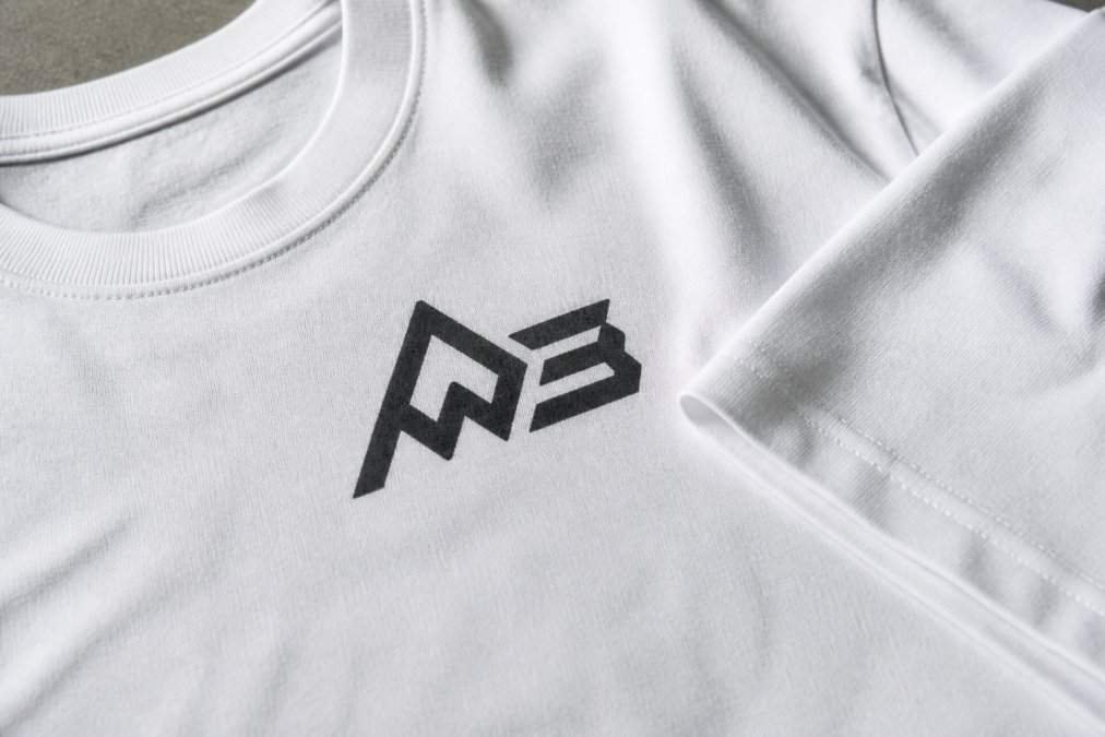 Close-up of heavyweight graphic tee fabric being examined, showing dense cotton weave, crisp DTG print detail, and reinforced double-needle stitching on collar and sleeve hems with natural studio lighting
