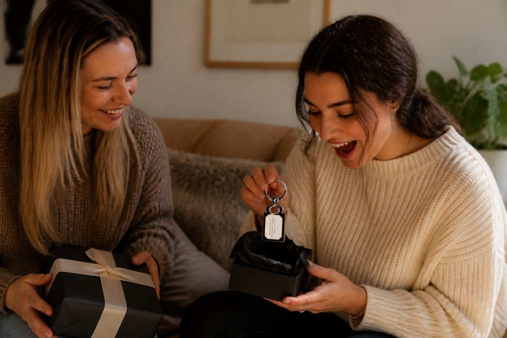 Two friends exchanging a wrapped gift in a cozy living room, one smiling as the other opens a personalized present with genuine joy and surprise