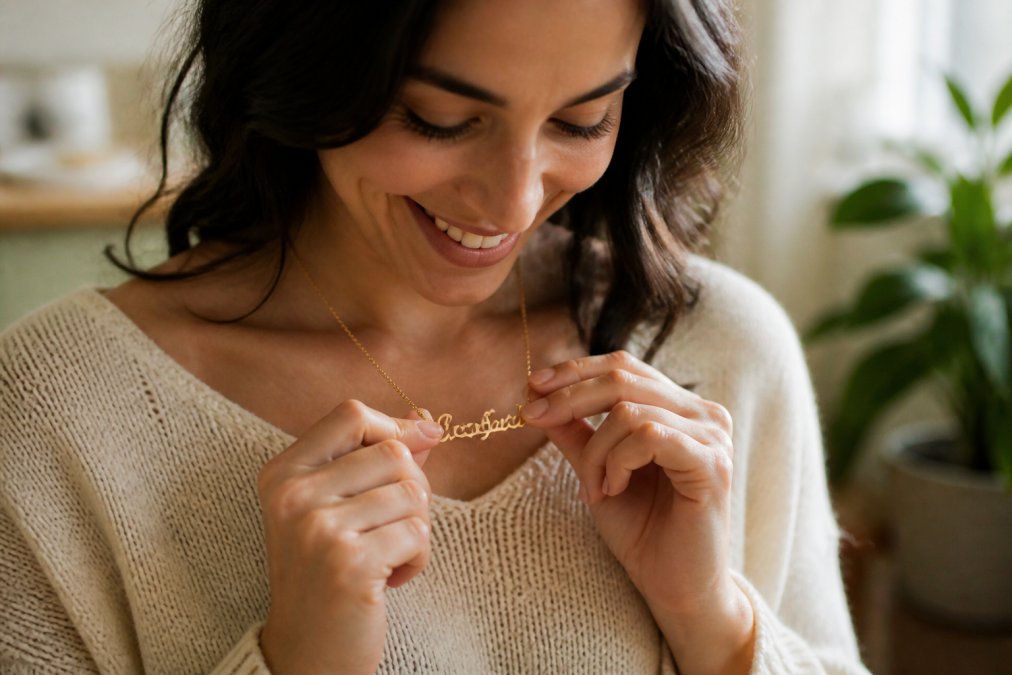A smiling woman holding a delicate personalized name necklace close to her heart as a meaningful gift