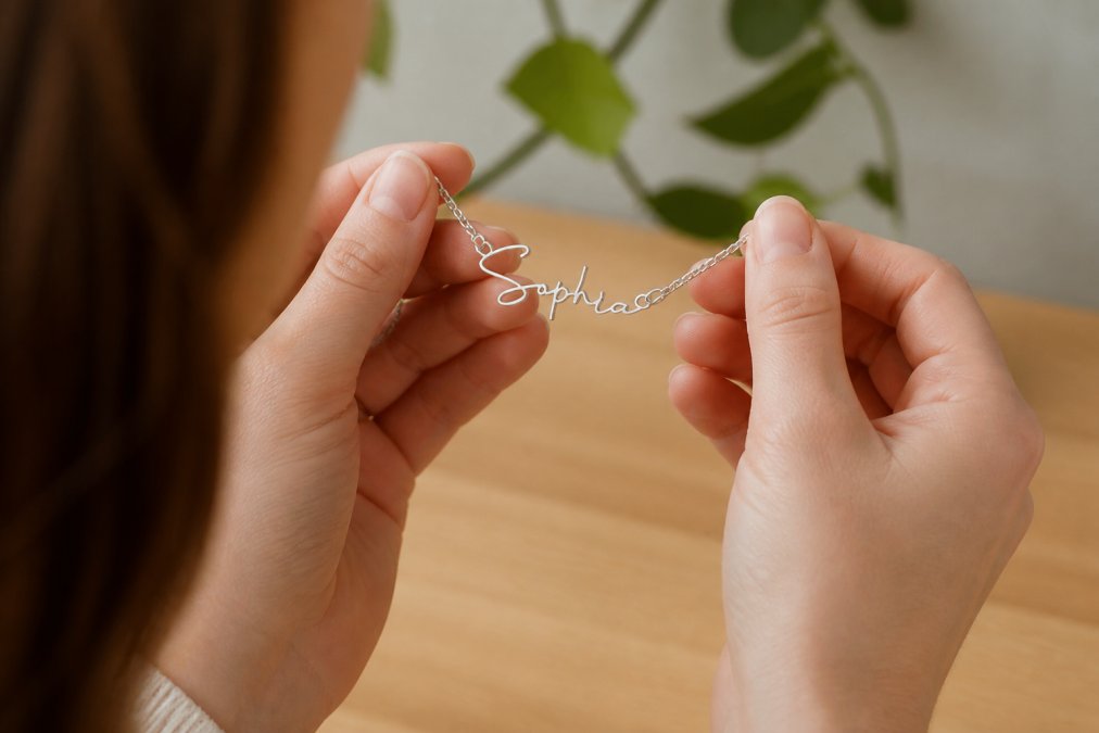 Close-up of hands carefully examining a personalized name necklace, studying the engraving with a thoughtful expression, showing the tactile quality and craftsmanship