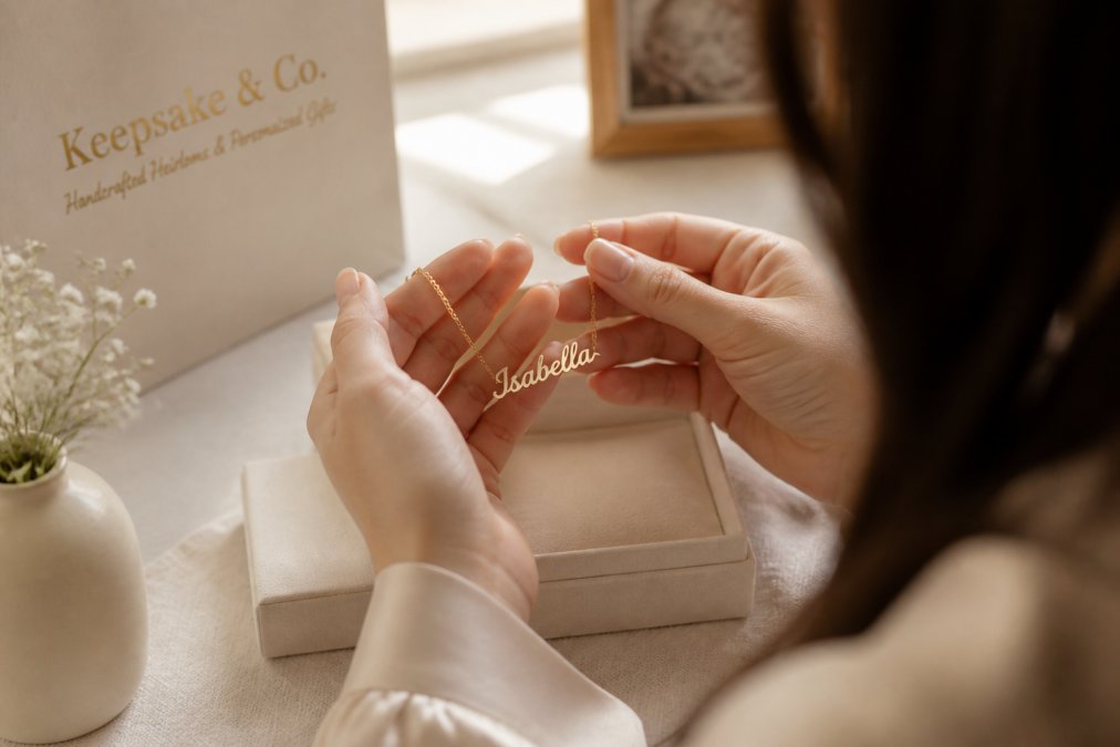 A close-up, warm photo of a woman's hands holding a delicate custom name necklace, with soft natural light and a blurred cozy background, capturing a moment of sentimental appreciation