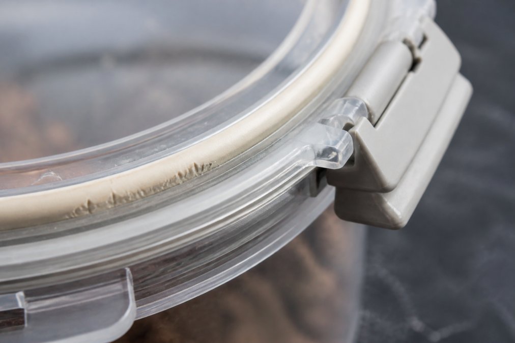 Close-up of a pet food container lid showing the gasket and latch mechanism with visible compression marks and wear on the rubber seal