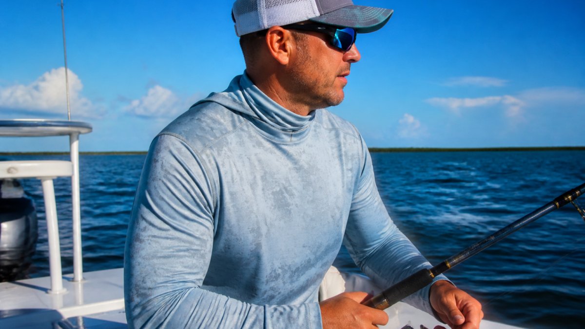 Angler in a high-performance fishing shirt on a boat during bright midday sun, showing the shirt's fit, fabric texture, and reinforced shoulder seams in action
