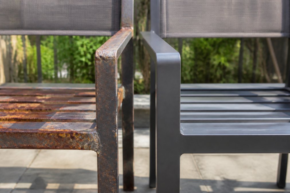 Close-up of weathered outdoor furniture showing rust forming on budget steel frame next to pristine powder-coated aluminum frame in bright afternoon sunlight, both exposed to elements