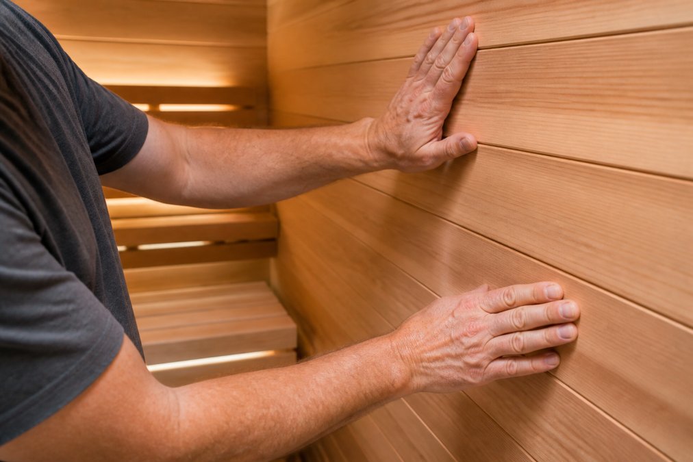 Craftsman touching smooth cedar planks inside one of our premium saunas with warm bench lighting