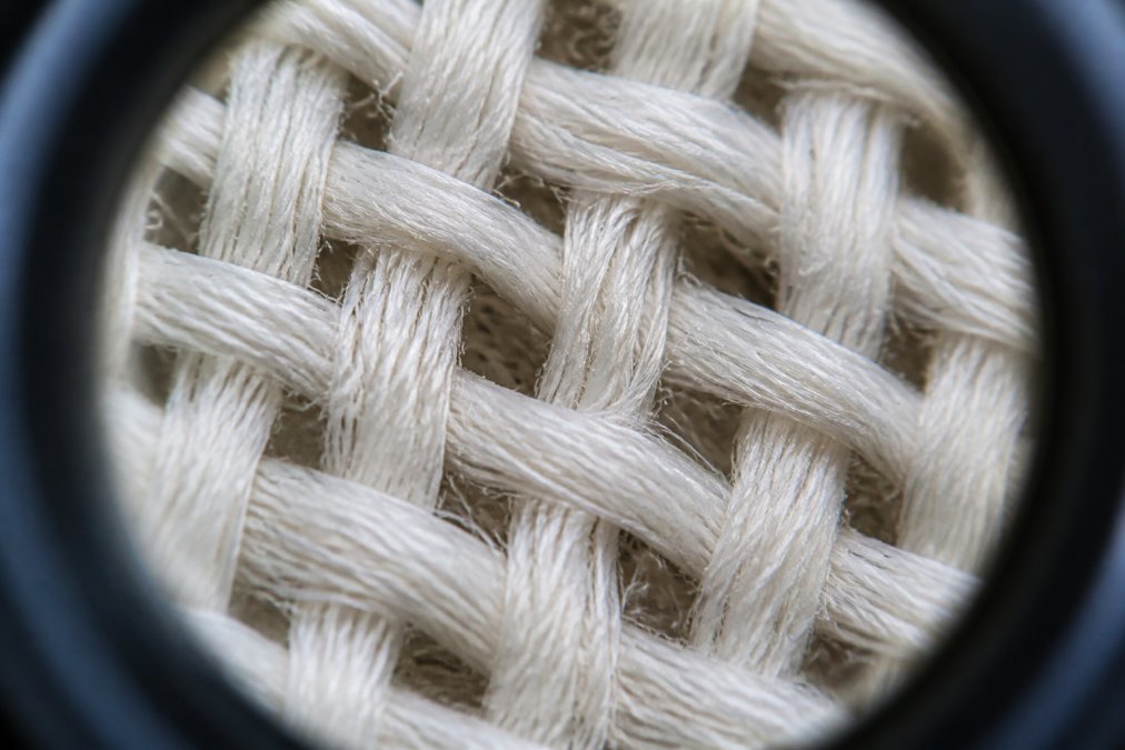 Close-up of premium cotton fabric fibers under magnification, showing the woven structure and tension in individual strands with natural daylight