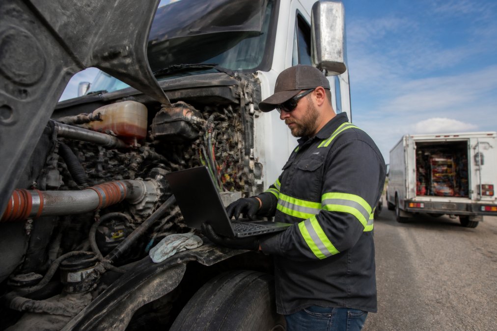 Diesel mechanic using diagnostic software on a laptop to perform preventive maintenance on a semi-truck engine.