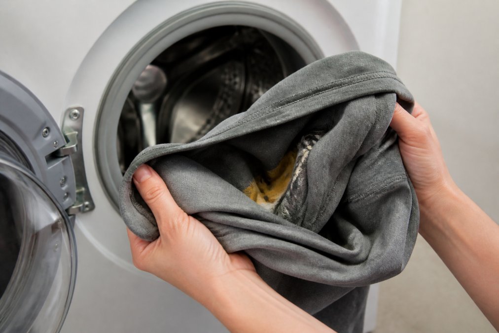 Close-up of hands turning a printed t-shirt inside out before placing it in a washing machine, showing the careful handling of the graphic design