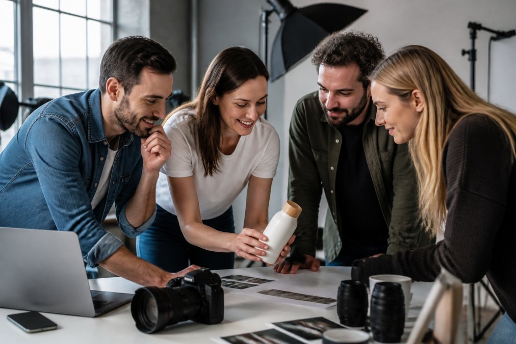 A marketing team reviewing a new product prototype on a clean studio table, with a professional camera and lighting equipment visible in the background