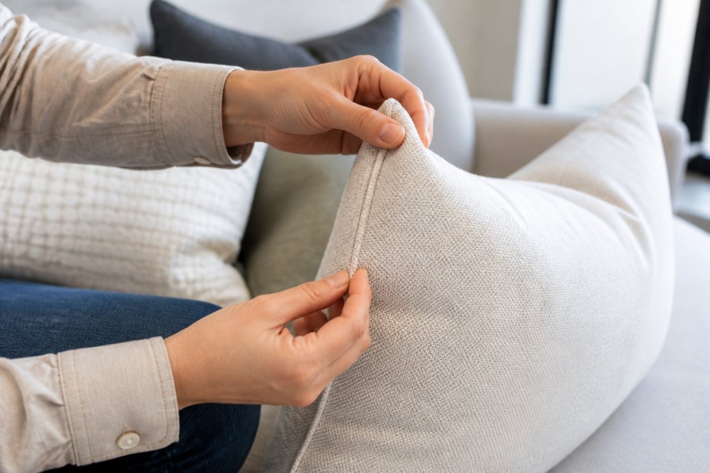 Close-up of hands examining seams, stitching detail, and fabric weight on a high-quality accent pillow, showing attention to construction with natural daylight highlighting the craftsmanship