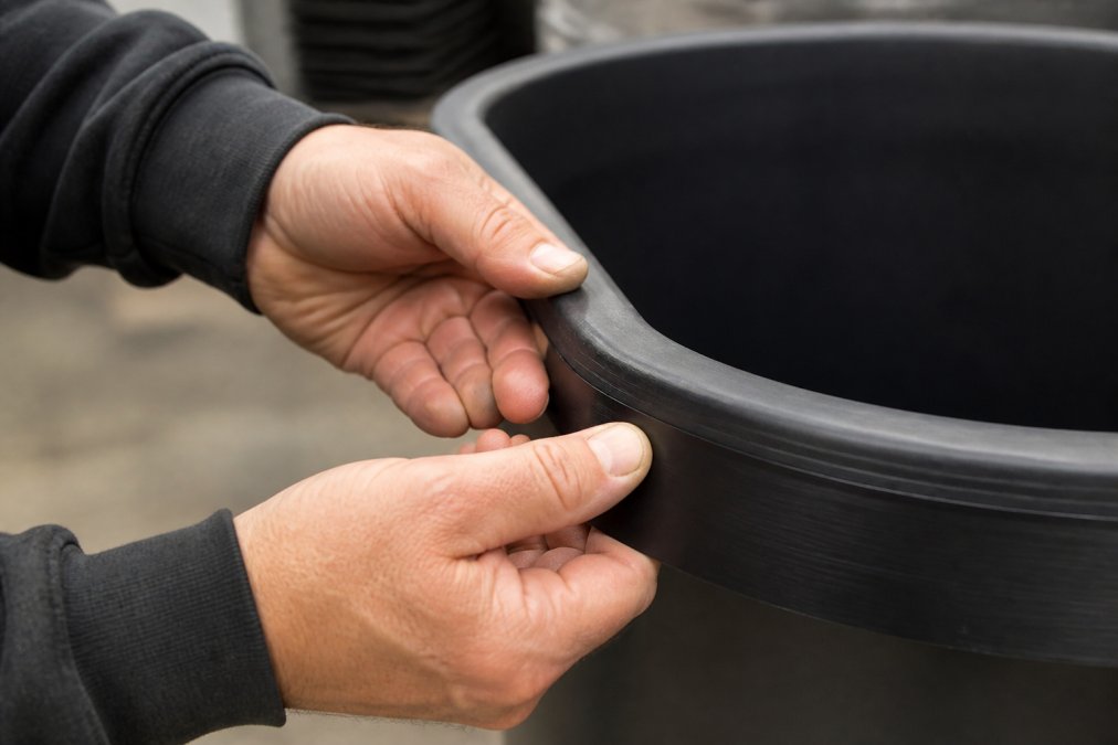 Close-up of hands examining the thick, durable wall of a large plastic planter, showing material density and construction quality
