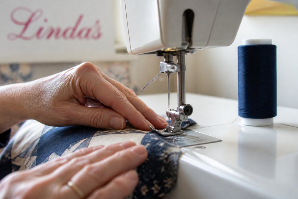 Quilter hands guiding fabric under a sewing machine needle with visible thread fraying near the eye