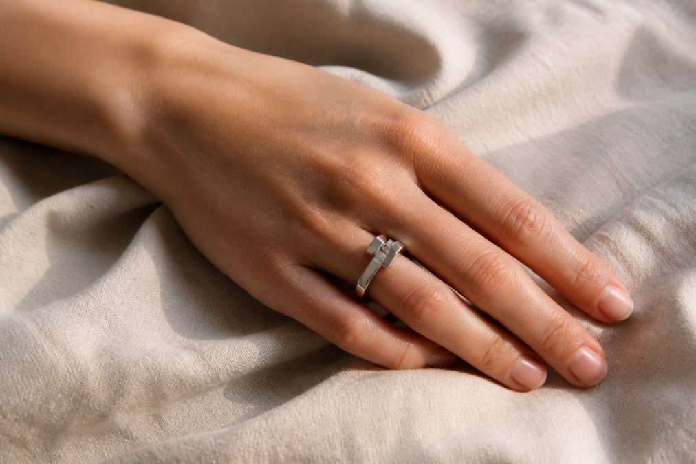 A woman's hand resting on a linen cloth, wearing a modern architectural platinum ring with a small diamond, soft window light catching the metal's natural white luster