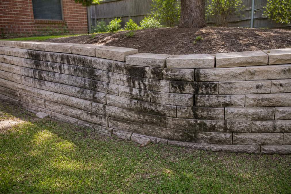 Diagram illustrating how poor retaining wall drainage causes bulging sections, cracked capstones, and water stains.