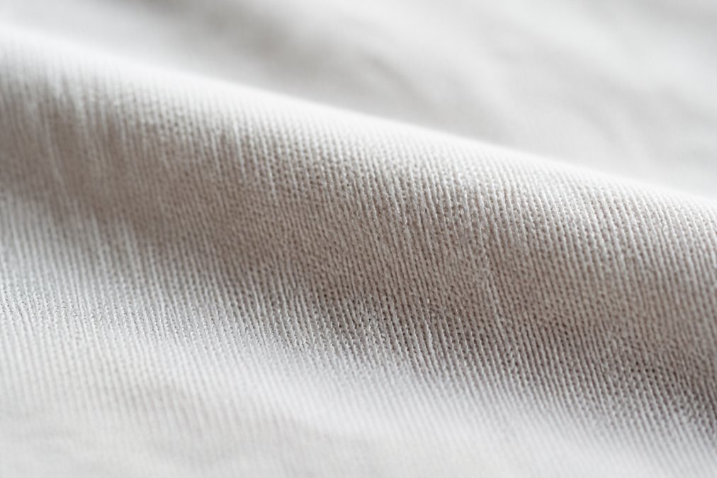 Close-up of premium soft cotton fabric texture with visible fiber alignment and smooth surface, natural light highlighting the refined yarn quality and tight fiber binding
