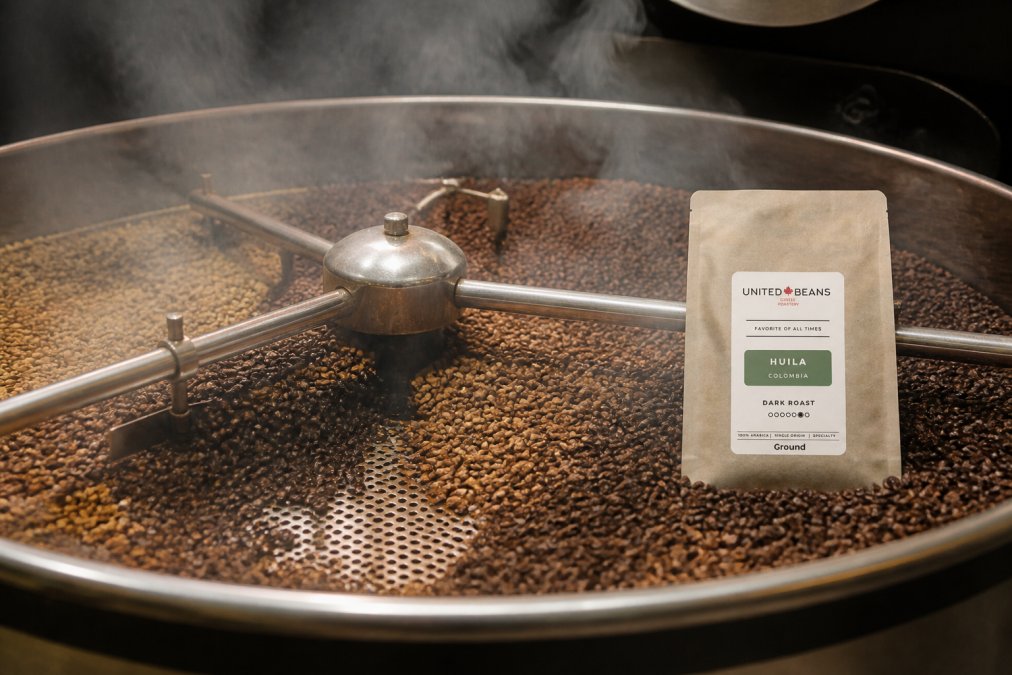 Freshly roasted specialty coffee beans tumbling in a cooling drum with visible steam rising, showing the full spectrum from light cinnamon to dark chocolate brown roast colors under warm industrial lighting