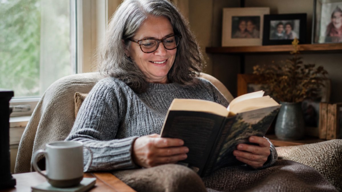 A reader smiles while enjoying a local author's book to support local independent authors in a cozy home setting.