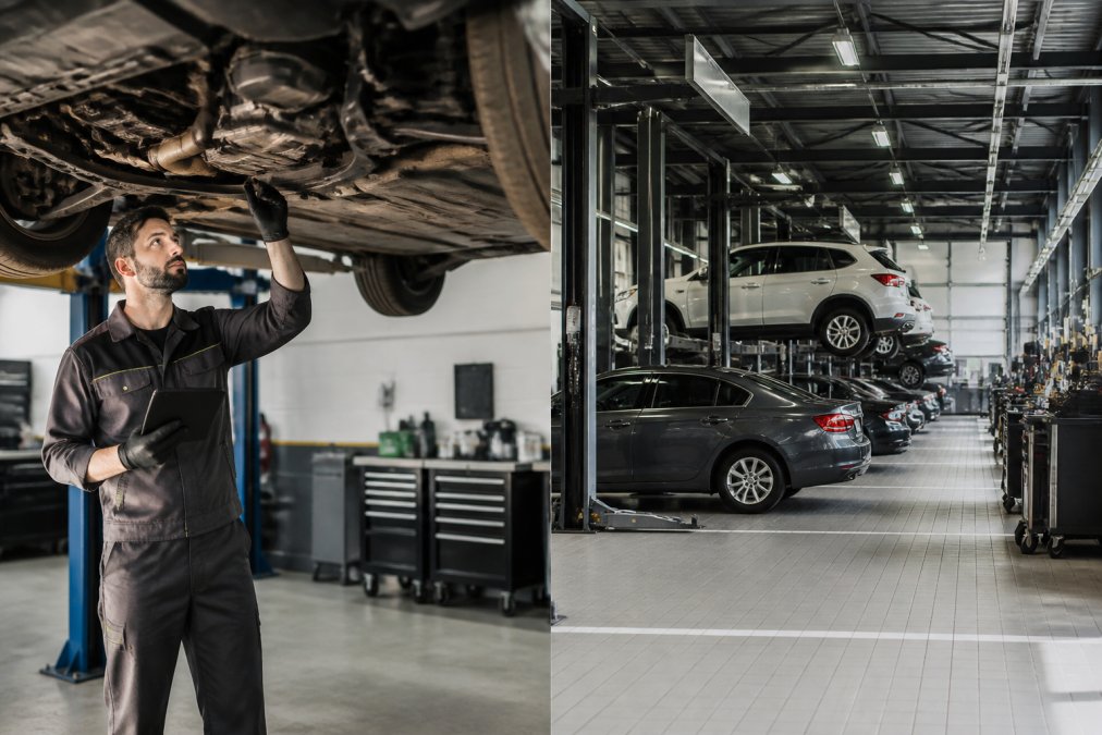 A certified mechanic in a clean, well-lit independent workshop inspecting the underside of a car on a hydraulic lift, wearing a uniform and holding a diagnostic tablet with one hand braced on the vehicle frame
