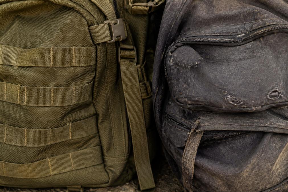 Close-up of weathered tactical backpack fabric showing reinforced stitching and abrasion-resistant material next to a worn budget backpack