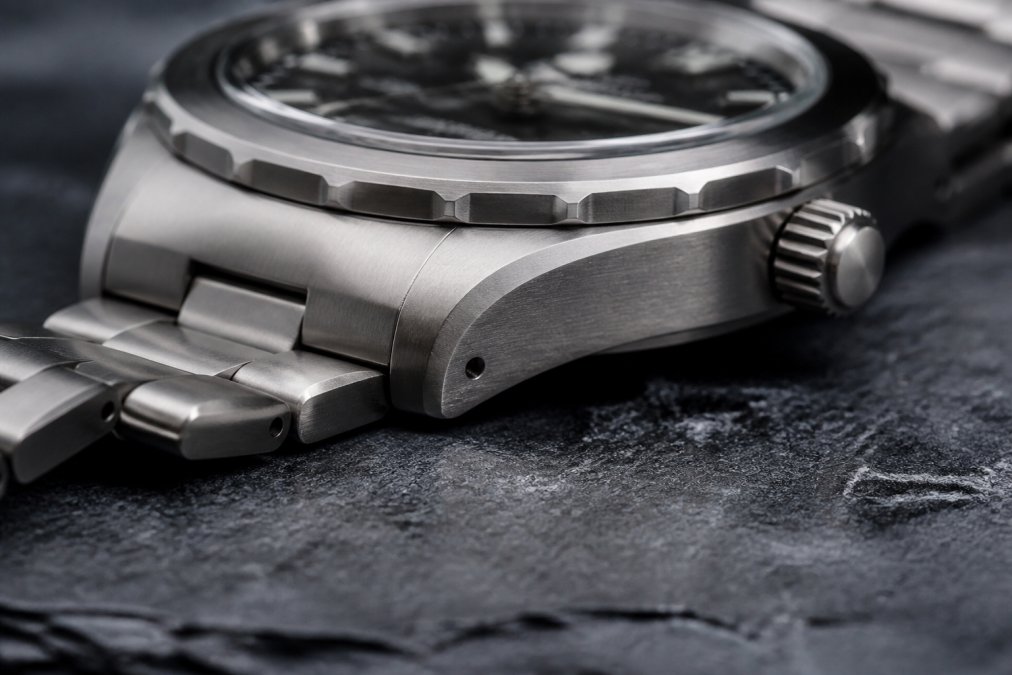 Close-up of a brushed titanium watch case and bezel resting on a dark slate surface, highlighting the matte metallic texture and refined finishing of the case construction