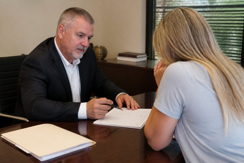 A professional bail bondsman in business attire sitting across a desk from a worried family member, reviewing paperwork together in a clean, well-lit office