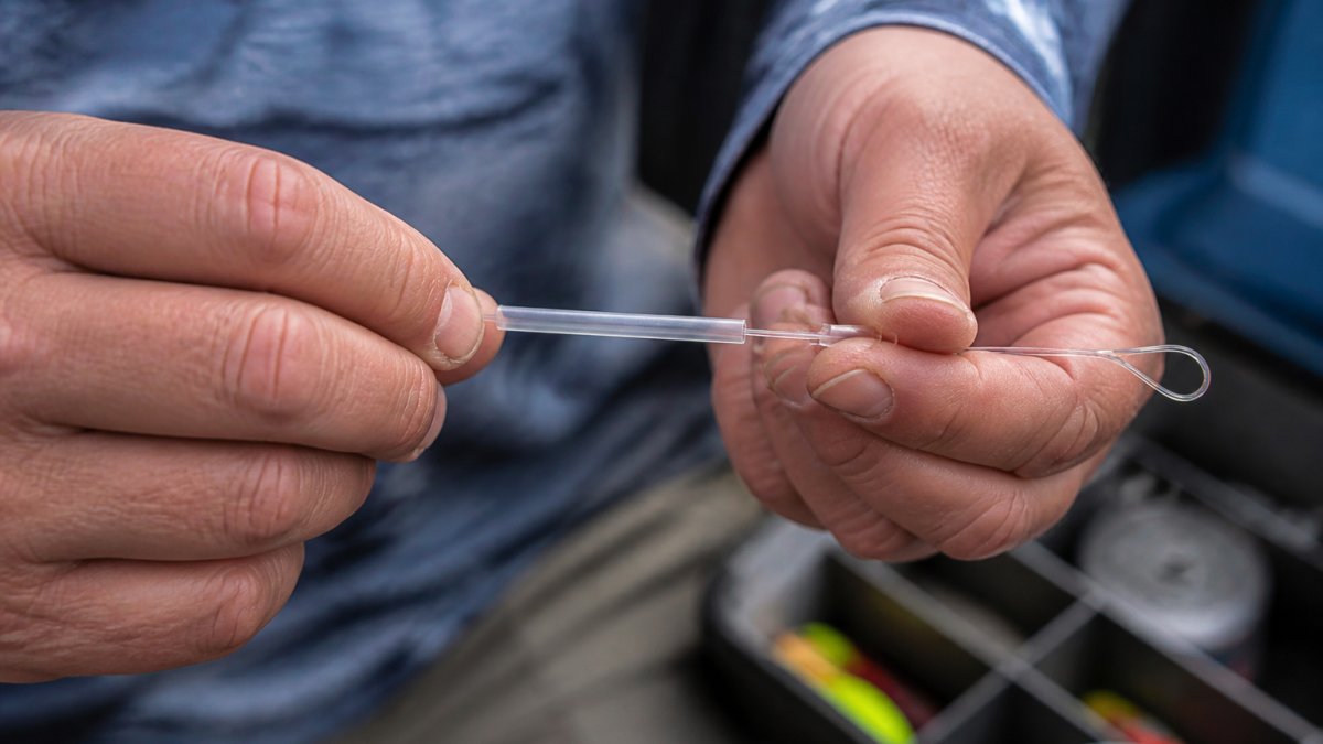 Angler's hands installing chafe tubing onto a monofilament leader near a loop connection, showing proper placement and snug fit with natural lighting