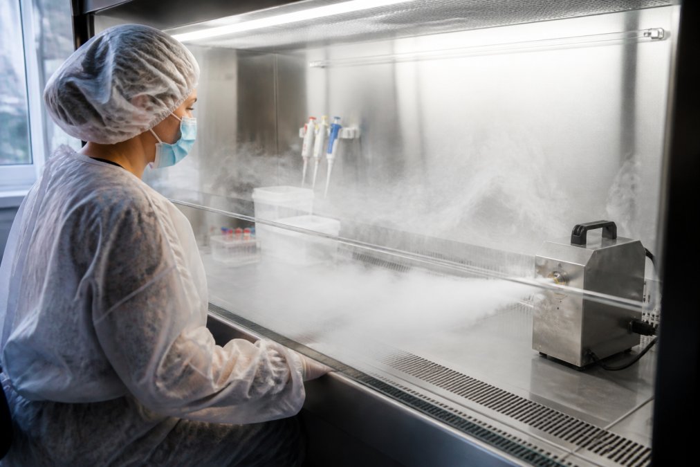 Quality assurance officer in sterile compounding pharmacy wearing protective equipment observing ultra-fine fog flowing across a biosafety cabinet work surface, with fog patterns clearly visible under bright lighting in a controlled pharmaceutical environment