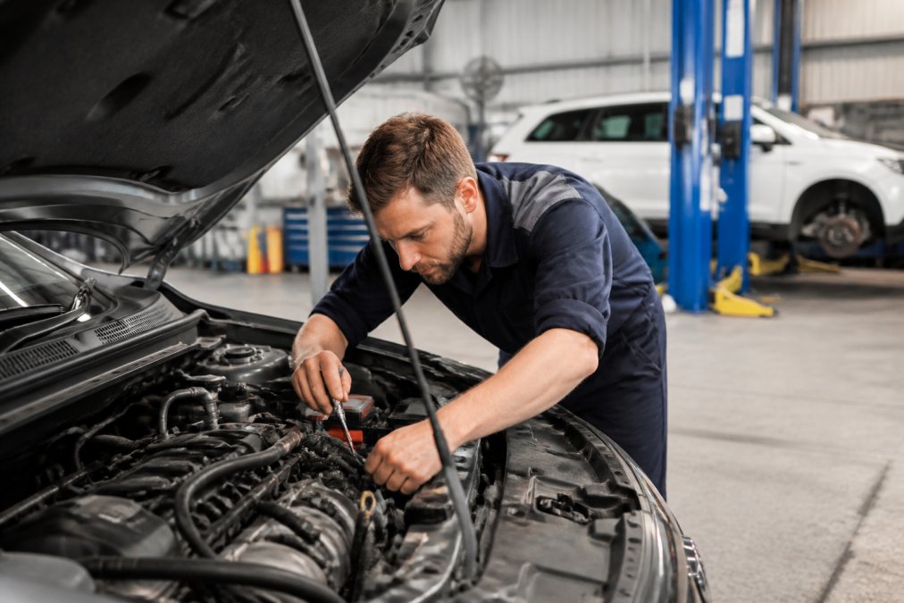Mechanic using diagnostic tools on a car engine in a modern workshop explains why vehicle repair costs are rising.