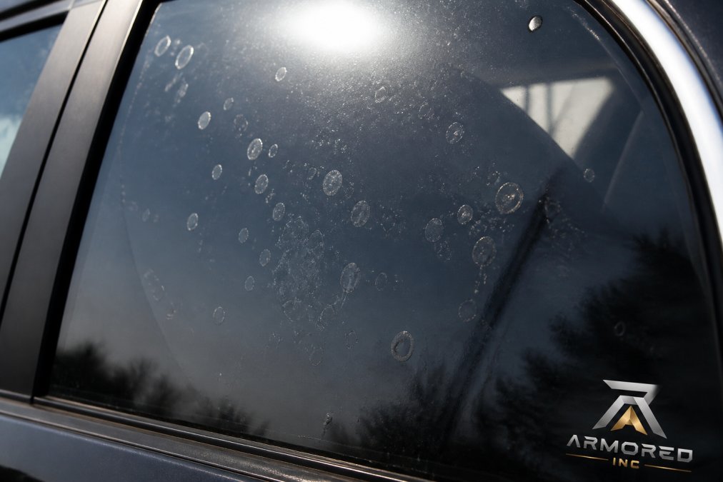 Close-up of a car window showing visible air bubbles and water pockets trapped beneath dark tint film, with sunlight highlighting the imperfections against the glass