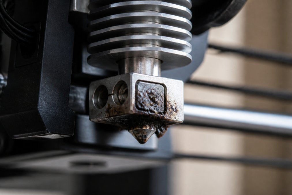 Close-up of 3D printer nozzle assembly showing the heating block, nozzle tip, and cooling fins with visible residue buildup on the nozzle surface