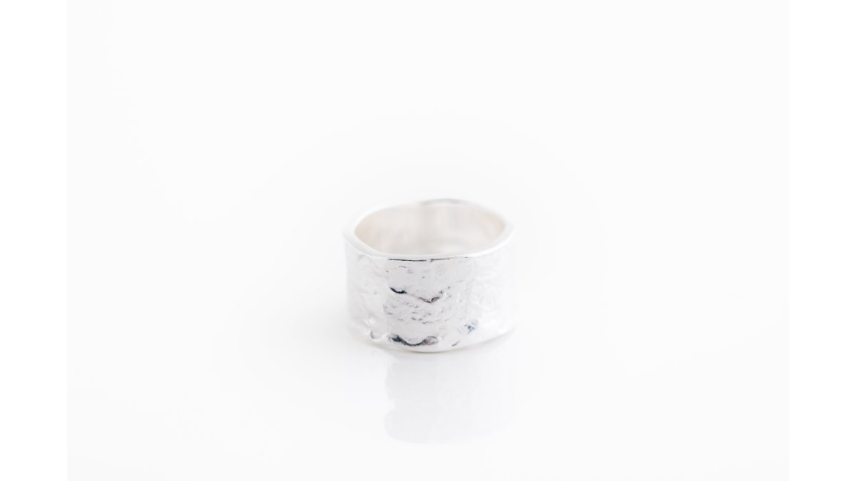 Close-up of a woman's hand and neck wearing a hammered sterling silver moon necklace and a wide silver band ring, soft natural window light, neutral background