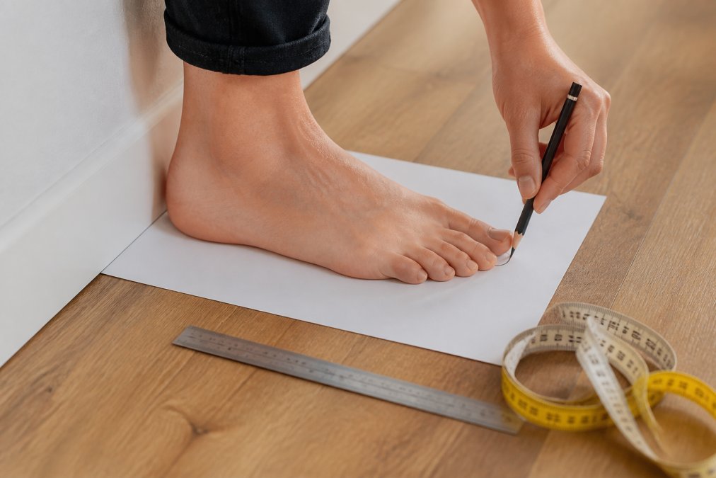 Person markiert auf einem Blatt Papier die Fußlänge, um die richtige Schuhgröße durch exaktes Messen zu bestimmen.