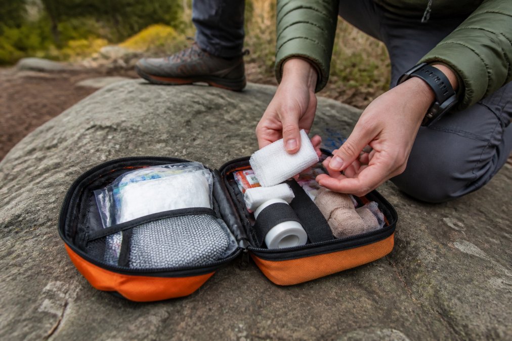 Hiker unpacking a compact first aid kit with medical supplies on a flat rock along a forest trail