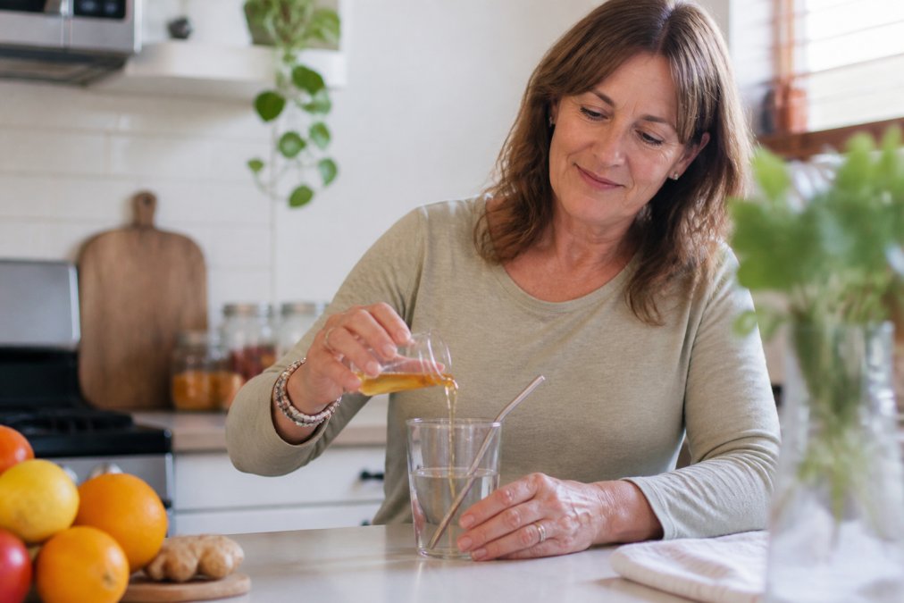 Woman in her 50s diluting an acv alternative in a glass of water in a bright kitchen