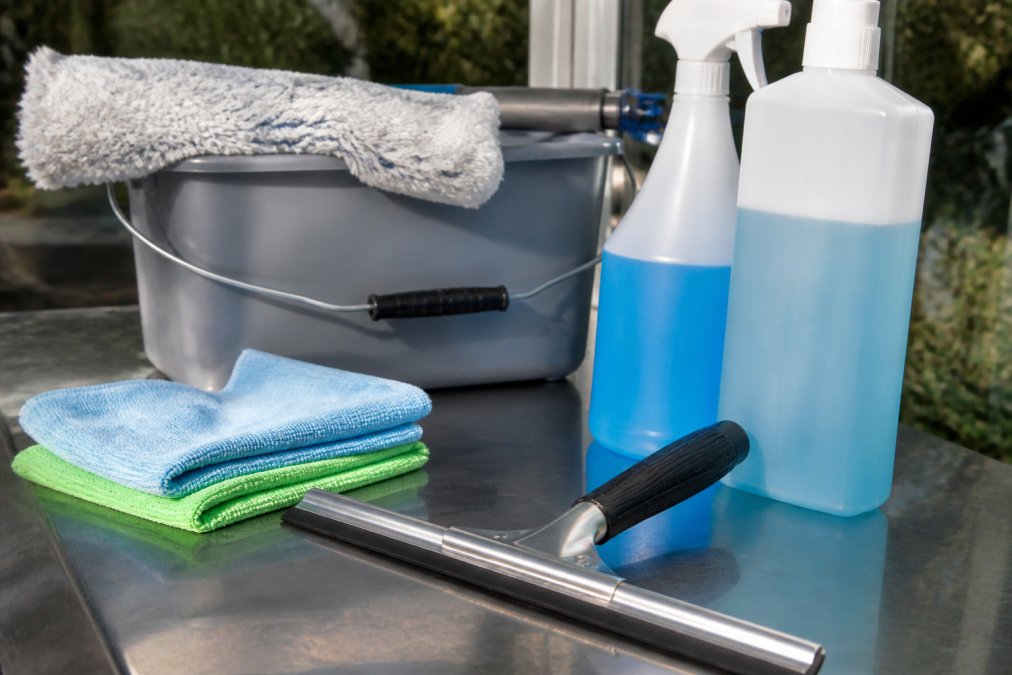 Close-up of professional window cleaning tools laid out including squeegee, microfibre cloths, bucket and cleaning solution bottles on a work surface