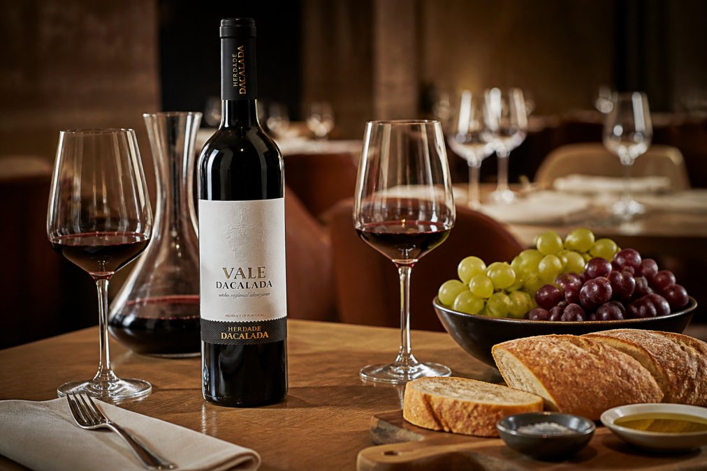 Restaurant table setting with Italian wine bottles and fine glassware arranged for service, showing premium Italian wines displayed with fresh grapes and bread on a wooden table in warm fine dining ambiance