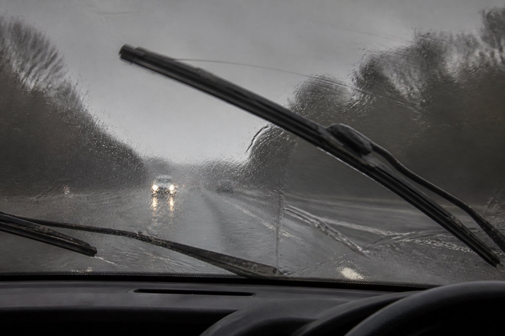 Close-up of worn windscreen wiper blades streaking across a wet windscreen during heavy rain, showing deteriorated rubber and poor visibility