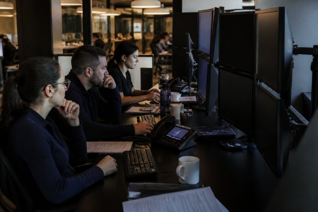 Security team reviewing AI agent logs and compliance dashboards on multiple monitors in a secure operations center with soft overhead lighting and multiple workstations