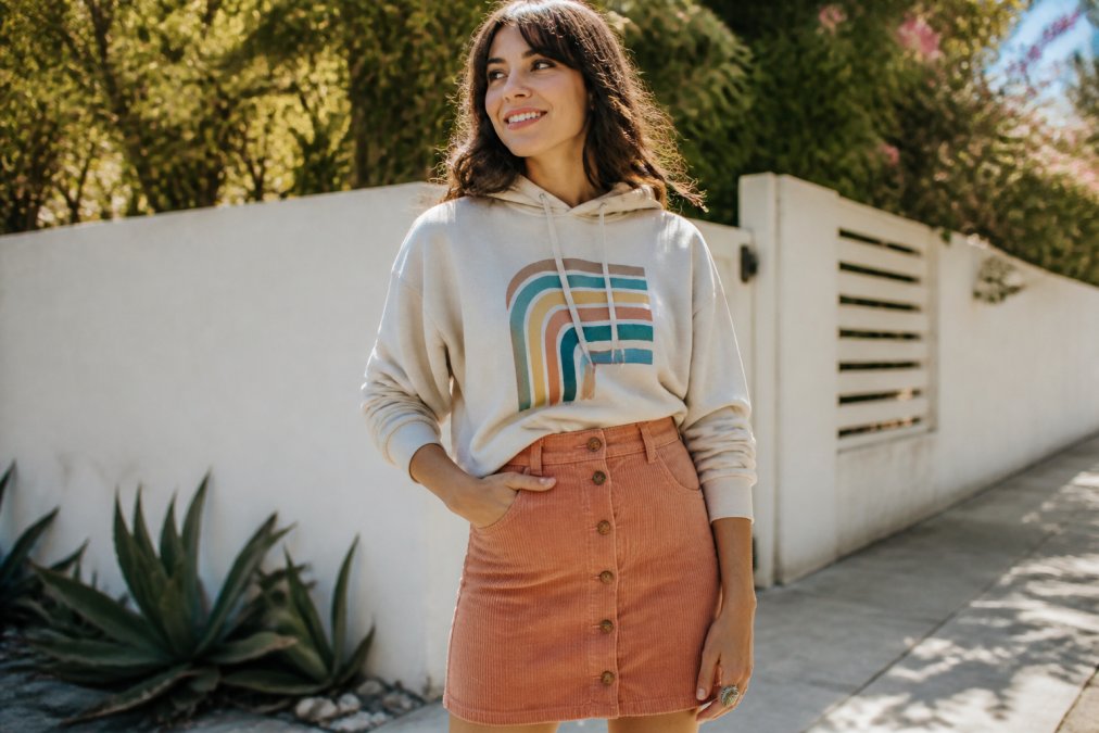 Woman wearing a high-waist corduroy skirt in apricot with a retro graphic hoodie, styled with a retro adjustable ring and natural spring daylight background