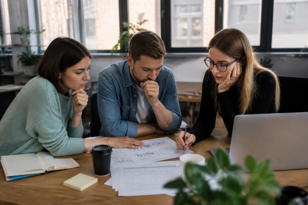 Startup-Team in modernem Büro sitzt zusammen vor mehreren Monitoren und analysiert Hosting-Kosten und Budgetplanungsspreadsheets mit konzentriertem Blick