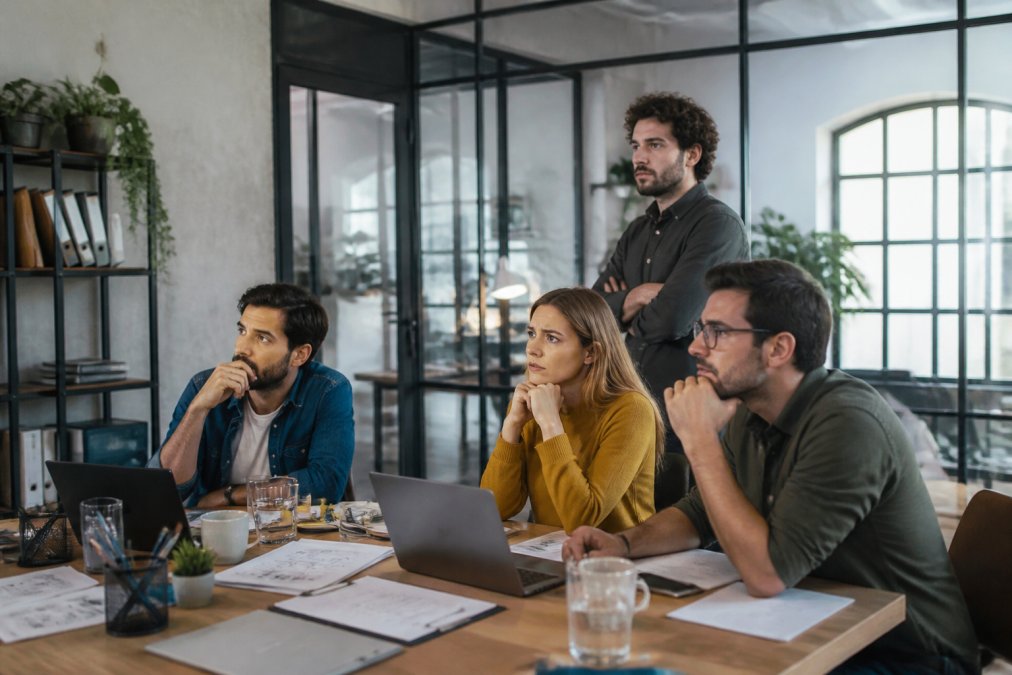 Mehrere Startup-Gründer in modernem Büro blicken auf große Monitore mit wachsenden Website-Traffic-Statistiken und Skalierungskurven, die nach oben zeigen