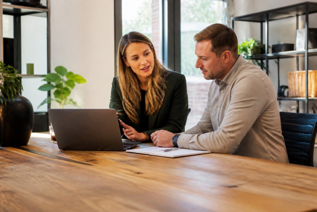 Ondernemer in gesprek met webdesigner, beiden kijkend naar een laptop met website-ontwerp op het scherm, in een professioneel kantooromgeving met natuurlijk licht