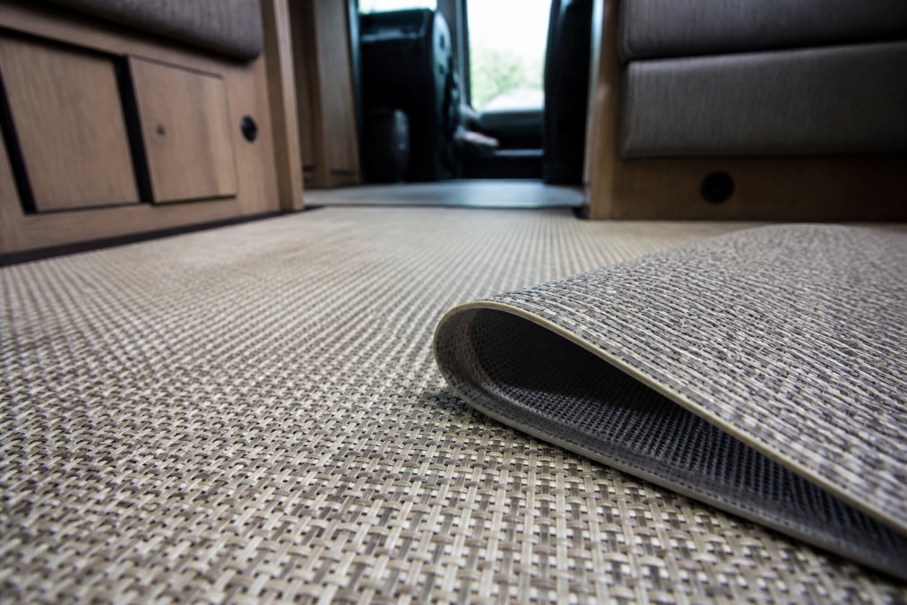 Close-up of woven vinyl flooring surface showing intricate weave texture and layered material construction in an RV interior with natural light highlighting durability features