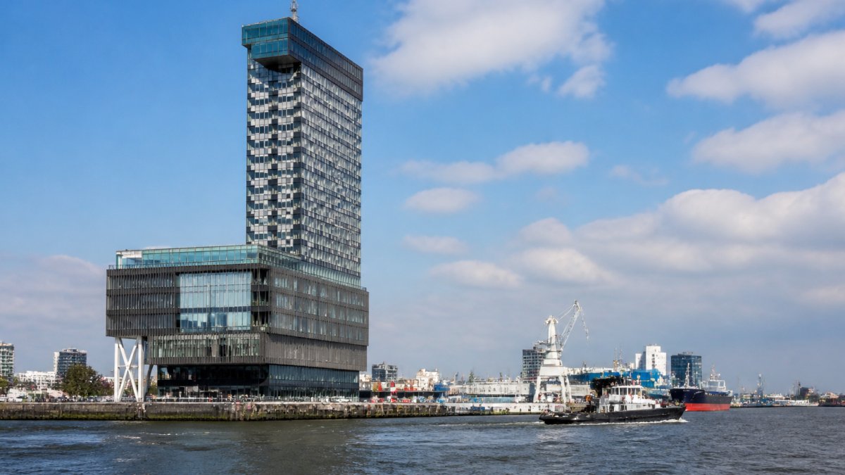 Uitzicht op het World Port Center-gebouw vanaf het water, met de 124 meter hoge toren zichtbaar tegen de skyline, havenactiviteiten en scheepsverkeer op de achtergrond