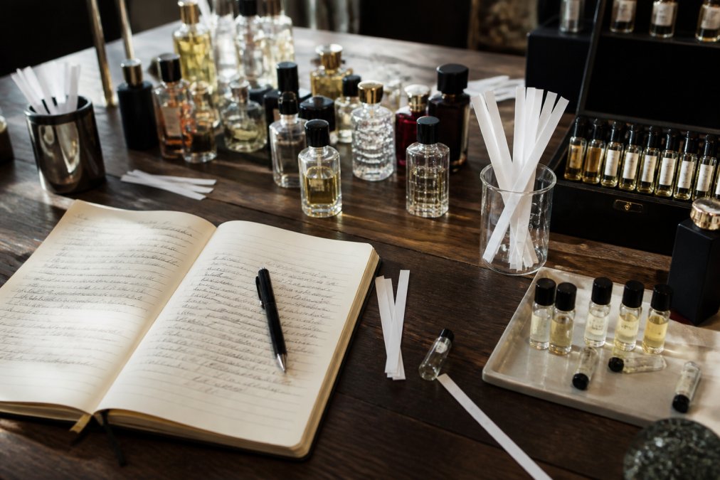 Fragrance collector's workspace with multiple open perfume bottles, sample vials, and a handwritten scent journal documenting personal curation and fragrance pairing notes