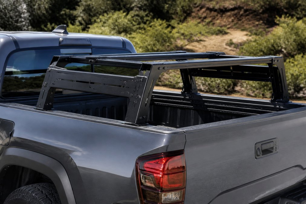 Close-up of a Toyota Tacoma truck bed with modular aluminum rack system installed, showing T-slot mounting channels and integrated accessory mounting points in bright daylight