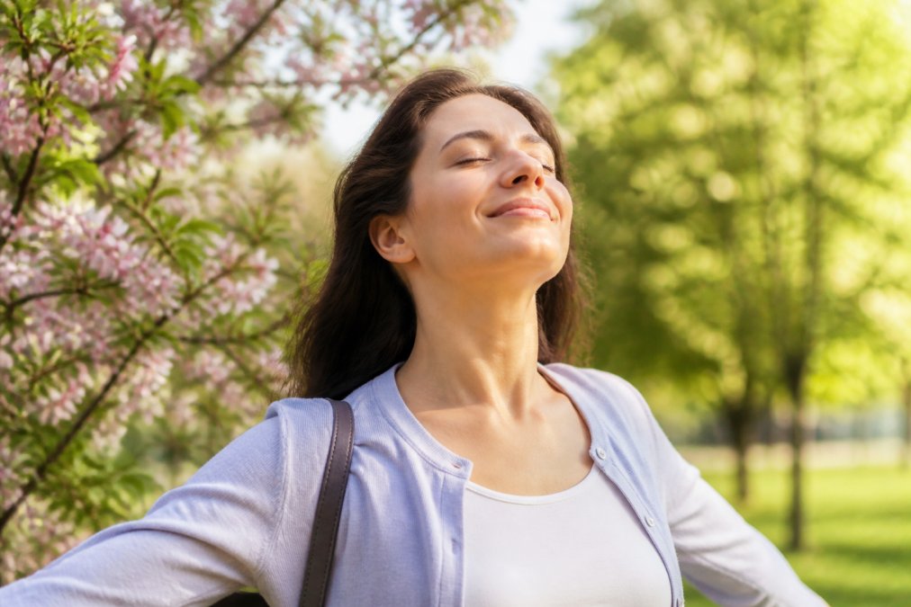 Person breathing clearly and comfortably outdoors during spring allergy season with green trees and flowers in background, appearing relieved and healthy with natural sunlight