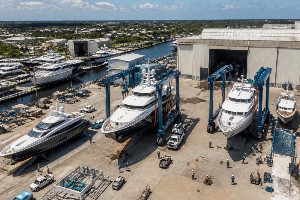 Aerial view of a large Florida shipyard with multiple yachts positioned on travel lifts and dry dock facilities, with professional workers coordinating refit work across the facility under bright daylight