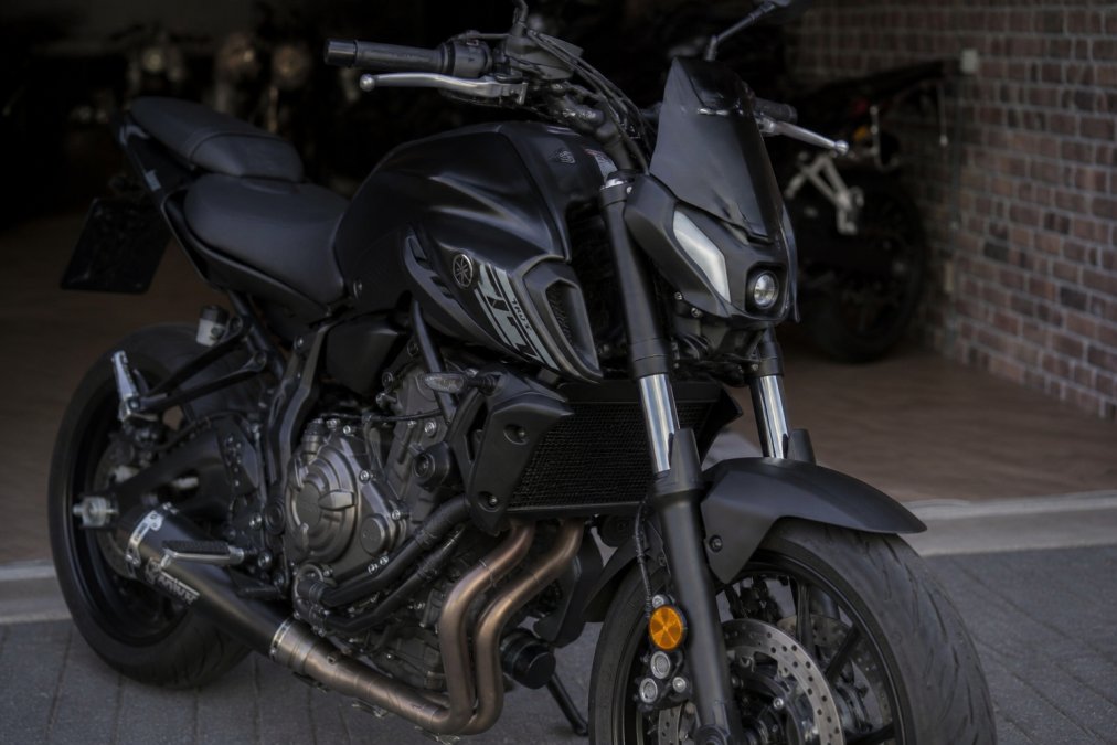 Close-up van de voorkant van een Yamaha MT-07 met scherpe LED-koplampen en radiaal gemonteerde remklauwen, detail op de omgekeerde voorvork en het stijve frame in natuurlijk licht