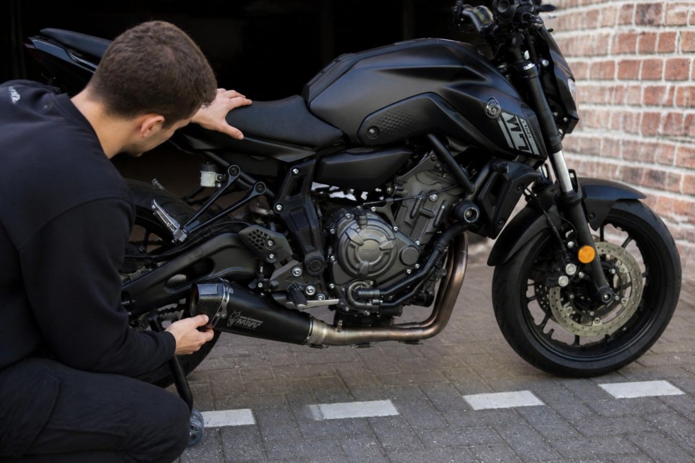 Handen van een motorrijder die de staat van een Yamaha MT-07 inspecteert, detail op de uitlaat, SpinForged velgen en frame in daglicht